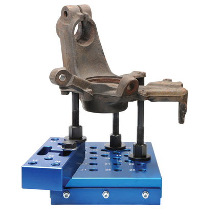 Blue universal press block with adjustable height anvil bolts shown pressing automotive suspension components securely.