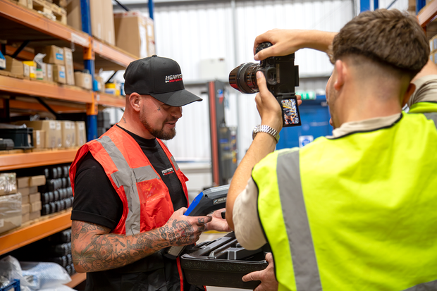 Person in a warehouse setting with another person taking a photo.